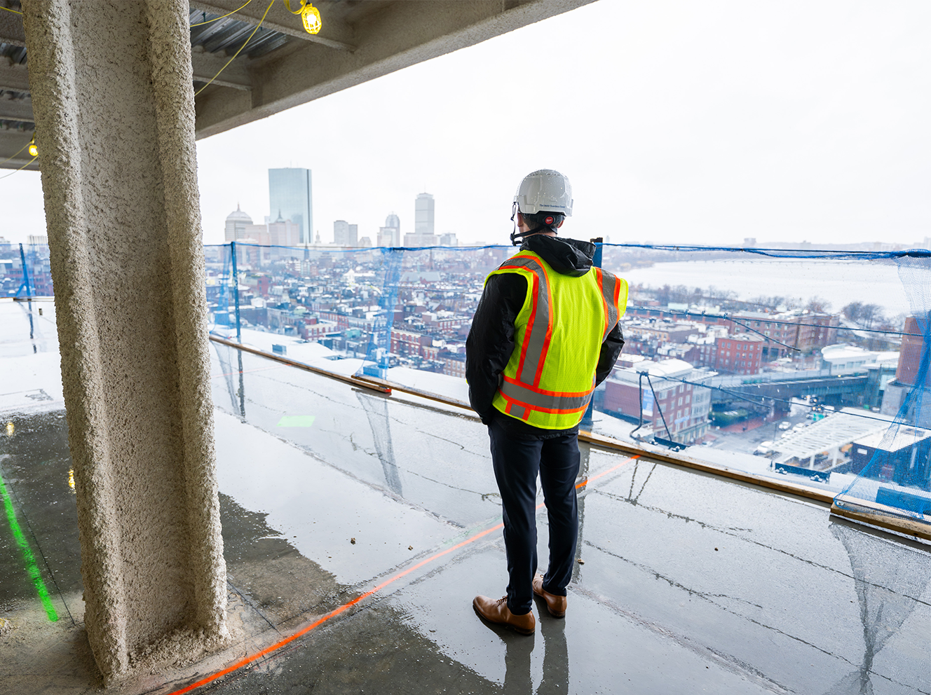 A man in construction saftey vest on a construction site overlooking Boston.