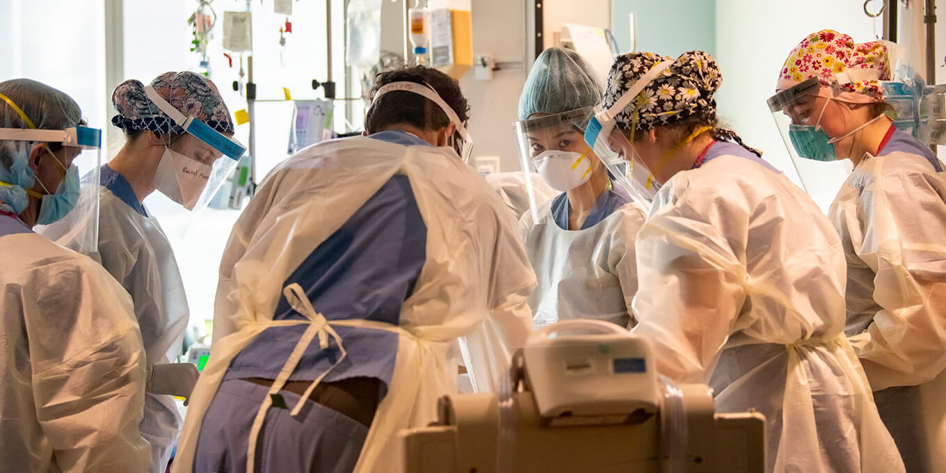 A group of nurses and care providers in protective gear gather to discuss a case